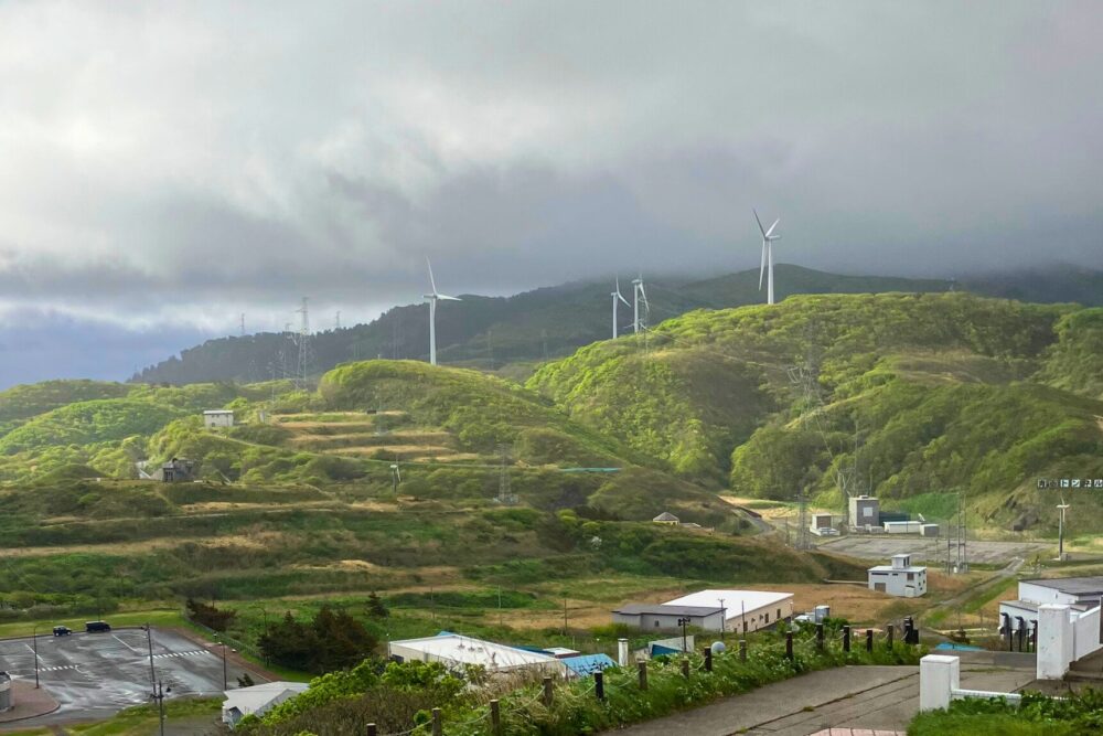 丘に建てられた風車が強風で回っている様子。