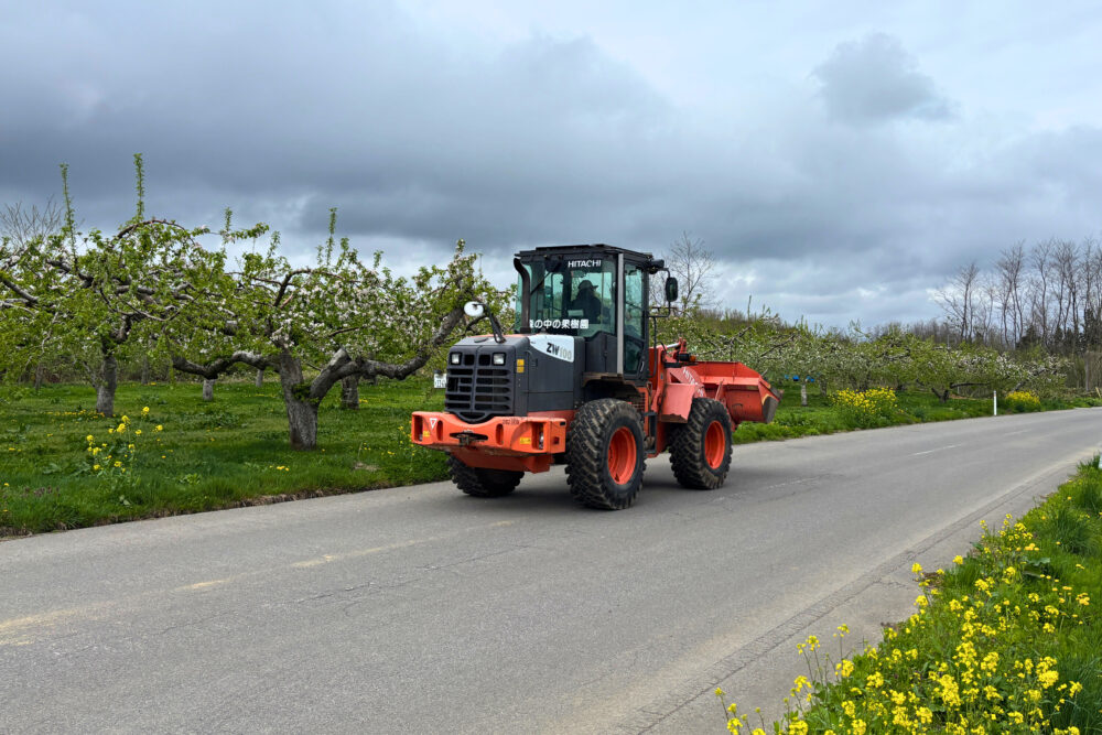 リンゴ畑に囲まれた道路を農作業車が走っているのどかな風景。