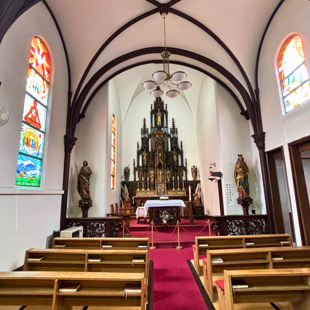 カトリック弘前教会の内観。正面に祭壇があり、壁面にはステンドグラス